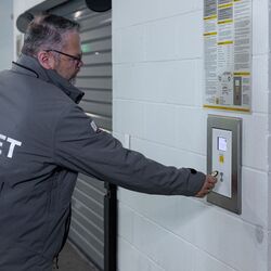 The image shows a person at the control panel of an automated parking system, confirming the storage process and thereby starting the automatic transport of the vehicle to an available parking space.