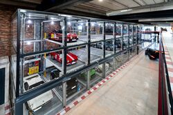 Vue en perspective du système de stationnement du Motorworld de Majorque, avec des voitures de sport exposées dans des vitrines