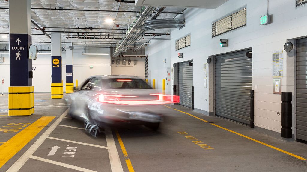 The image shows a vehicle entering an automated parking system within a modern underground garage with several access gates.