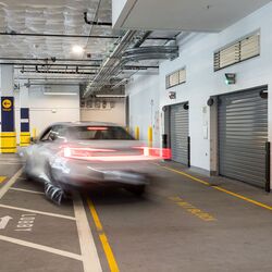 The image shows a vehicle entering an automated parking system within a modern underground garage with several access gates.