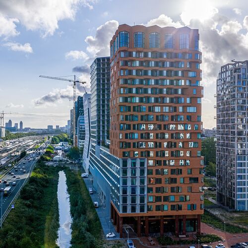 Vue extérieure du projet The Pulse à Amsterdam avec des immeubles de grande hauteur modernes et des infrastructures de transport urbain.
