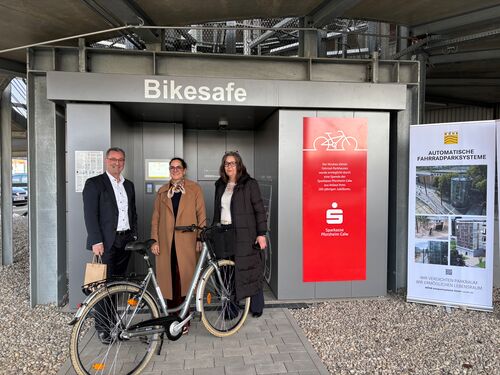 Trois personnes se tiennent devant l'entrée du système de stationnement automatique pour vélos, un vélo à la main